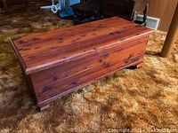 Top-side angle view of cedar blanket chest showing wood grain, natural knots, and low feet on carpeted floor.
