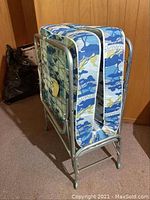 Photo of folded metal frame folding bed with mattress in blue and white camouflage pattern.