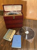 Set of 30 records in storage box with 2 course books placed beside the box on a wooden surface, showing overall lot contents and condition.