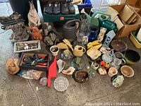 Full overview of assorted garden decor, planters, vases, watering cans, and shoes laid out on the ground