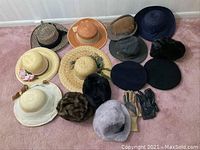 Photo showing assortment of hats and gloves arranged on carpet, including straw, fabric, and faux fur hats, along with leather and fabric gloves.