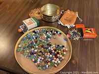 Full lot overview including marbles in a round tray, jacks, tins, drawstring pouch, and decorative bowl