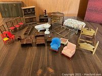 Front view of all miniature doll house furniture arranged on wood surface showing chairs, bed, porcelain tub and sink, and various wooden dressers and tables
