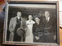 Full view of framed black and white photo showing four men with autographs and inscriptions on the photo surface.