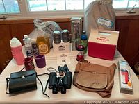 Full view of all items arranged on table for listing, showing thermos, binoculars, Aerobed, lanterns, cooler, drink containers and bags.