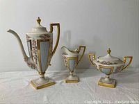 Front view of teapot, creamer, and sugar bowl set on white cloth background