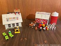 Overview of both schoolhouse and farm barn playsets with accessories on a wooden table against a wood panel wall.