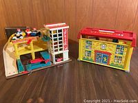 Photo of the main parking ramp playset with elevator and child figures seated in cars on the ramp. Separate yellow and red building resembling a children's hospital visible.