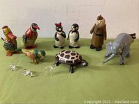 Front view of entire lot showing the colorful vintage tin litho windup toys including duck, parakeet, turtle, along with penguin salt and pepper shakers labeled Millie and Willie, wooden soldier figure, plastic elephant by Revell, and 3 miniature clear glass animal figurines (camel, hippopotamus, flamingo).