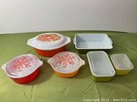 Photo showing all six vintage Pyrex casseroles and baking dishes on green surface, with colorful lids and patterns visible.