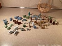 Wide shot showing the assortment of Wade miniature ceramic animal figurines laid out on a flat surface next to a small woven basket.