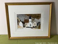 Framed acrylic artwork showing a winter village scene with white houses and a church steeple, by Rene M Verleyrn.