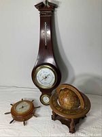 Two wood and brass barometers and a small wood globe displayed on white surface against plain background.