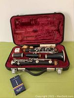 Full view of vintage Yamaha clarinet disassembled and placed in a red velvet lined carrying case along with a Yamaha branded reed box and polishing cloth.