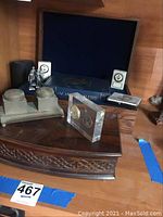 Front view showing carved wooden box, acrylic paperweight, desk clocks, figurines, book and tapes.