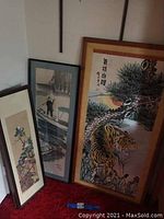 Three framed Asian art prints shown together leaning against a wall. Includes large tiger print with Chinese calligraphy, medium person on boat print, and smaller floral print.