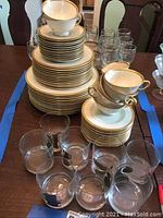 Stack of Lenox Tuxedo china plates and soup bowls on table with assorted glassware behind