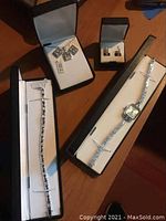Top view of the bracelet, necklace with charms, earrings, and watch in their boxes
