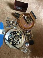 Overview of the lot including jewelry, cufflinks, coins, spoons, decorative plates, and a wristwatch on a carpeted floor.