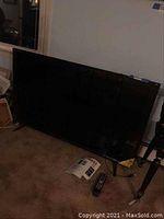 Front view of TV on floor showing screen and included remote and manual in front