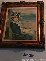 Frontal view of framed painting showing a lady in a chair by the shore, with details of the frame ornate decoration.
