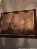 Framed painting showing two sailing ships on the ocean with cloudy sky, captured from front angle showing frame details.