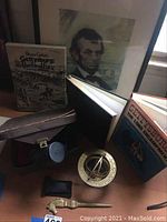 Overview photo showing Gettysburg books, Abraham Lincoln photo, brass sundial compass, telescope, small magnifying glass, and brass letter opener on table near window.