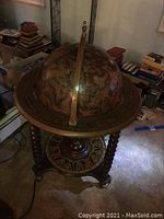 Full view of the decorative globe bar on wooden stand with carved legs and geometric patterned lower shelf.
