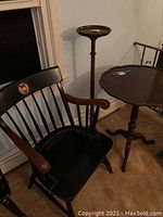 Hitchcock black armchair, wooden plant stand, and round wooden table in a corner