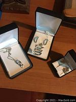 Three black jewelry boxes containing a necklace, a set of rings, and a pair of earrings on a wooden surface.