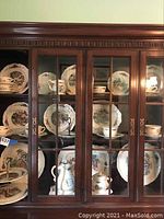 China cabinet shelf displaying multiple plates, cups and serving pieces