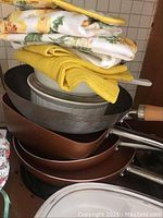 Stack of three frying pans, oven towels, and pot holders with wooden and metal handles visible