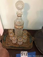 Cut glass decanter with stopper and six small matching glasses on an embroidered fabric tray