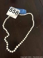 Full view of pearl necklace laid on a dark surface showing round pearls and a clasp.