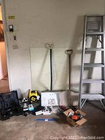 Full view of lot showing two snow shovels, aluminum ladder, power tools in cases, Stanley power hub, power strips, hammer, and assorted small tools.