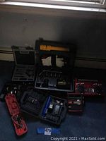 Wide photo showing multiple tool kits, air compressor, gloves, and two retro radios on the floor near a wall baseboard and window.