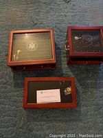 Three wooden coin collector boxes on blue carpet, showing their tops with glass protective covers and wooden frames