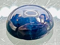 Close-up images of the oval cabochon cut blue star sapphire showing the domed smooth surface, reflections, and star asterism effect.