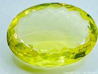 Close up photo of a large oval cut canary yellow lemon quartz gemstone showing its faceting and color saturation.