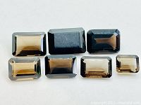 Seven emerald cut smokey quartz gemstones arranged in two rows, showing color and faceting detail.