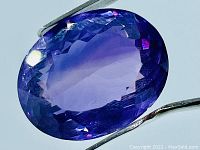 Close-up image of the oval cut deep purple Amethyst held by tweezers showing its facets and luster.