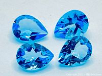 Four beautifully faceted pear shape Swiss blue Topaz gemstones arranged closely on white background, showing clarity and bright faceting.