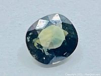 Close-up image of cushion cut multicolor greenish purple Songea Tanzania sapphire showing faceted surface and natural color variation.