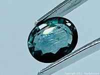 Close-up of the green oval cut sapphire held in tweezers, showing faceted top and color.