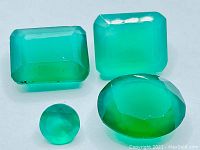 Four lime green onyx gemstones of mixed cuts and sizes shown together on white background highlighting color and clarity