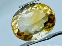 Close-up image of a 6.78 ct golden oval cut citrine held by tweezers showing facets and transparency