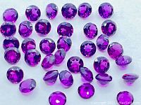 Close-up photo of the pink purple Rhodolite Garnet round faceted gemstones, showing their color and cut.