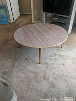Full view of the round table on carpet, showing table top and legs, highlighting simple mid-century modern design and height.