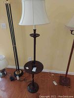Full view of the wooden floor lamp showing the lampshade, round tray, and base on hardwood floor near other floor lamps.