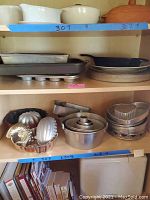 Shelf with bakeware including bundt pans, loaf pans, cake pans, molds, and Calphalon cast iron fry pan